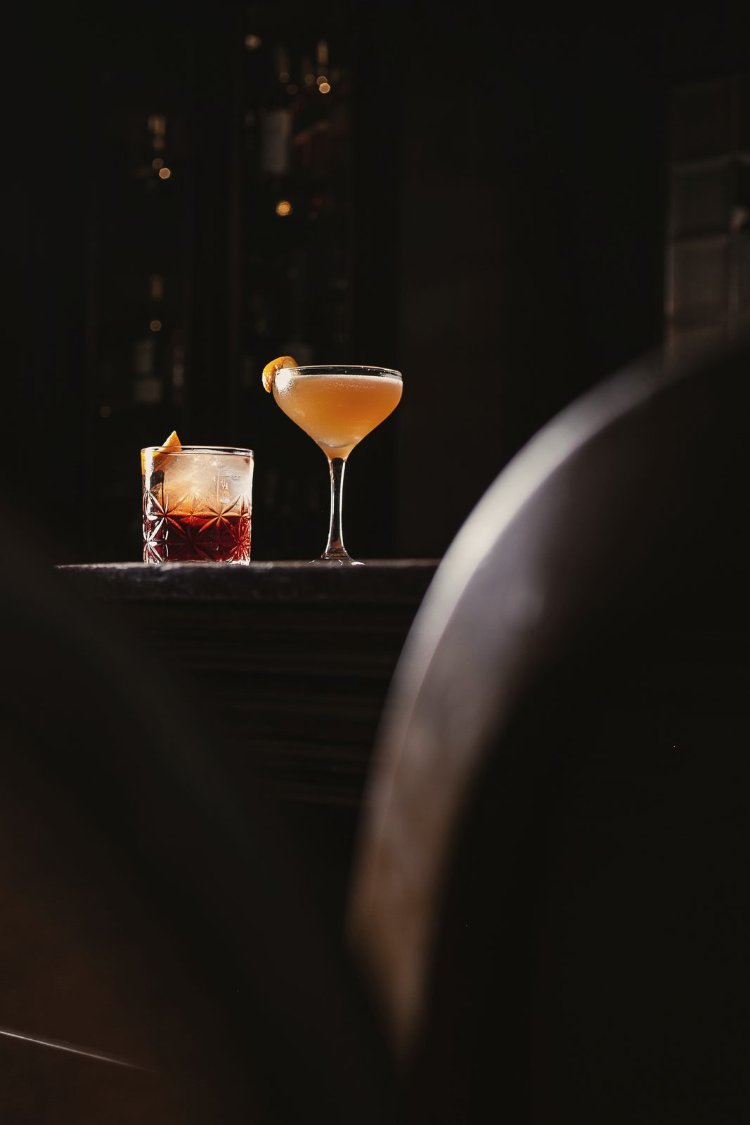 Dois drinks sobre um móvel escuro, em penumbra